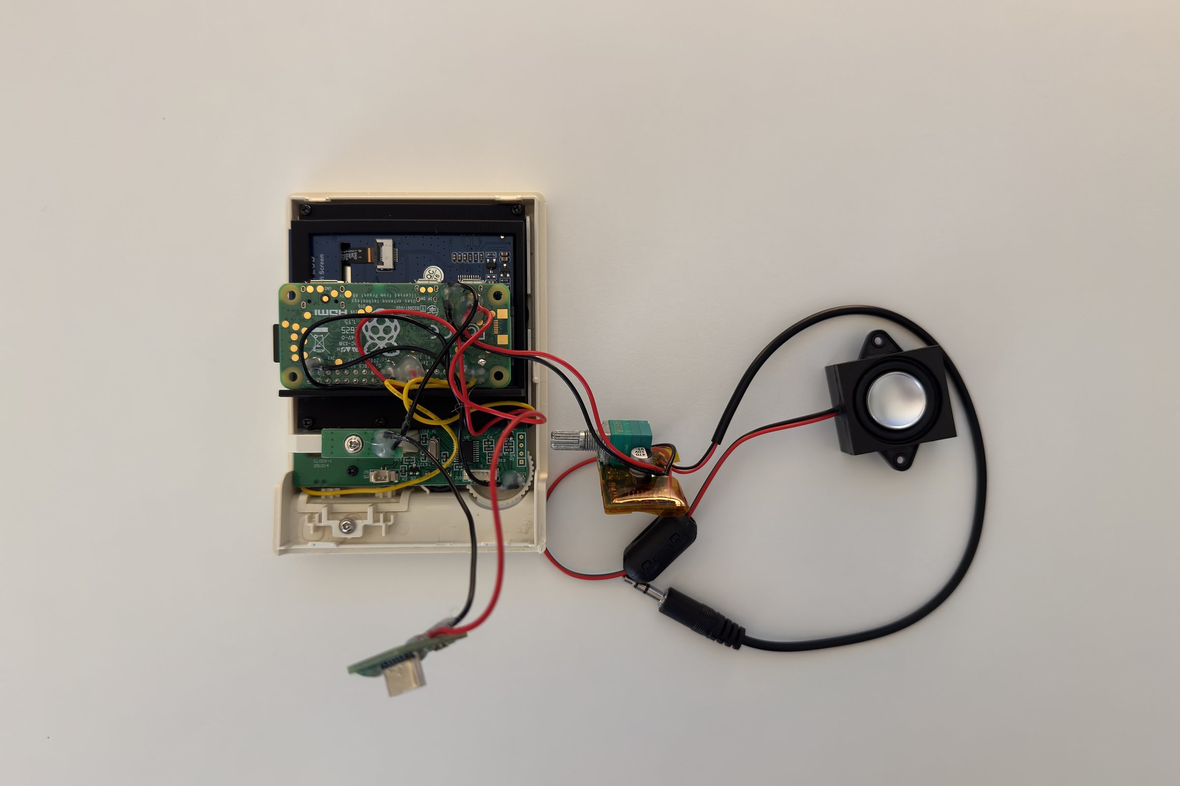 The assembly laid flat: the shell front holding the Pi and display, wired to an amplifier board, a USB audio adapter, and a speaker