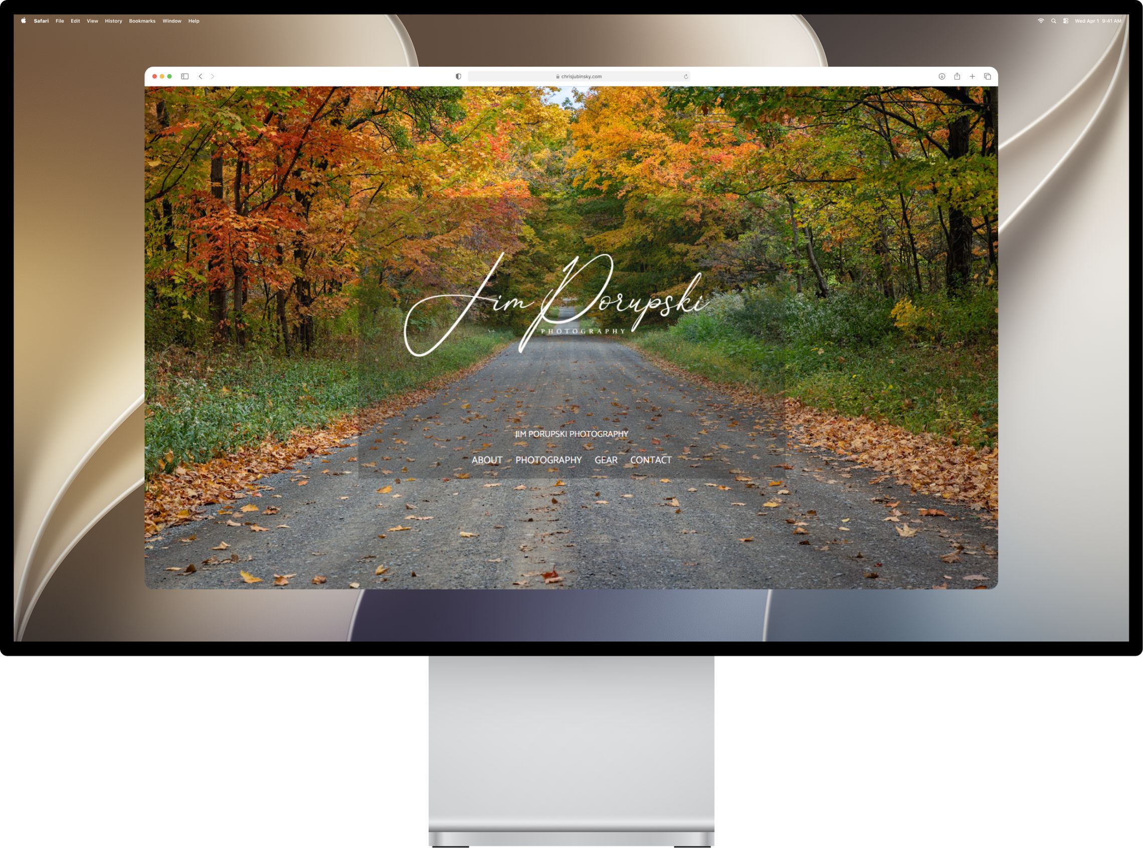 The photography site's homepage on a desktop monitor, a full-width autumn road photograph behind the studio name and nav
